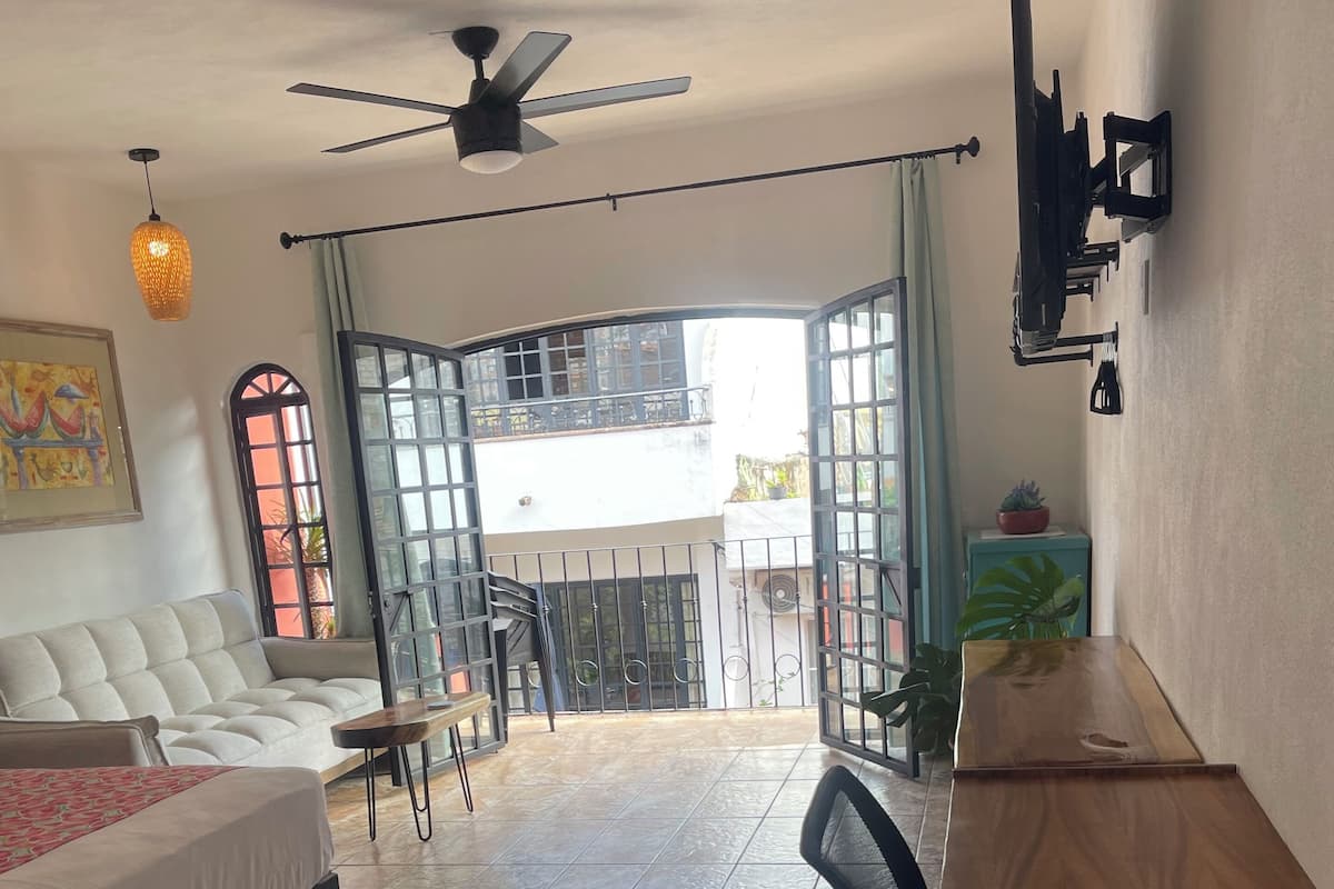A room with a bed, a desk, a chair, a ceiling fan, and a view of the outside.