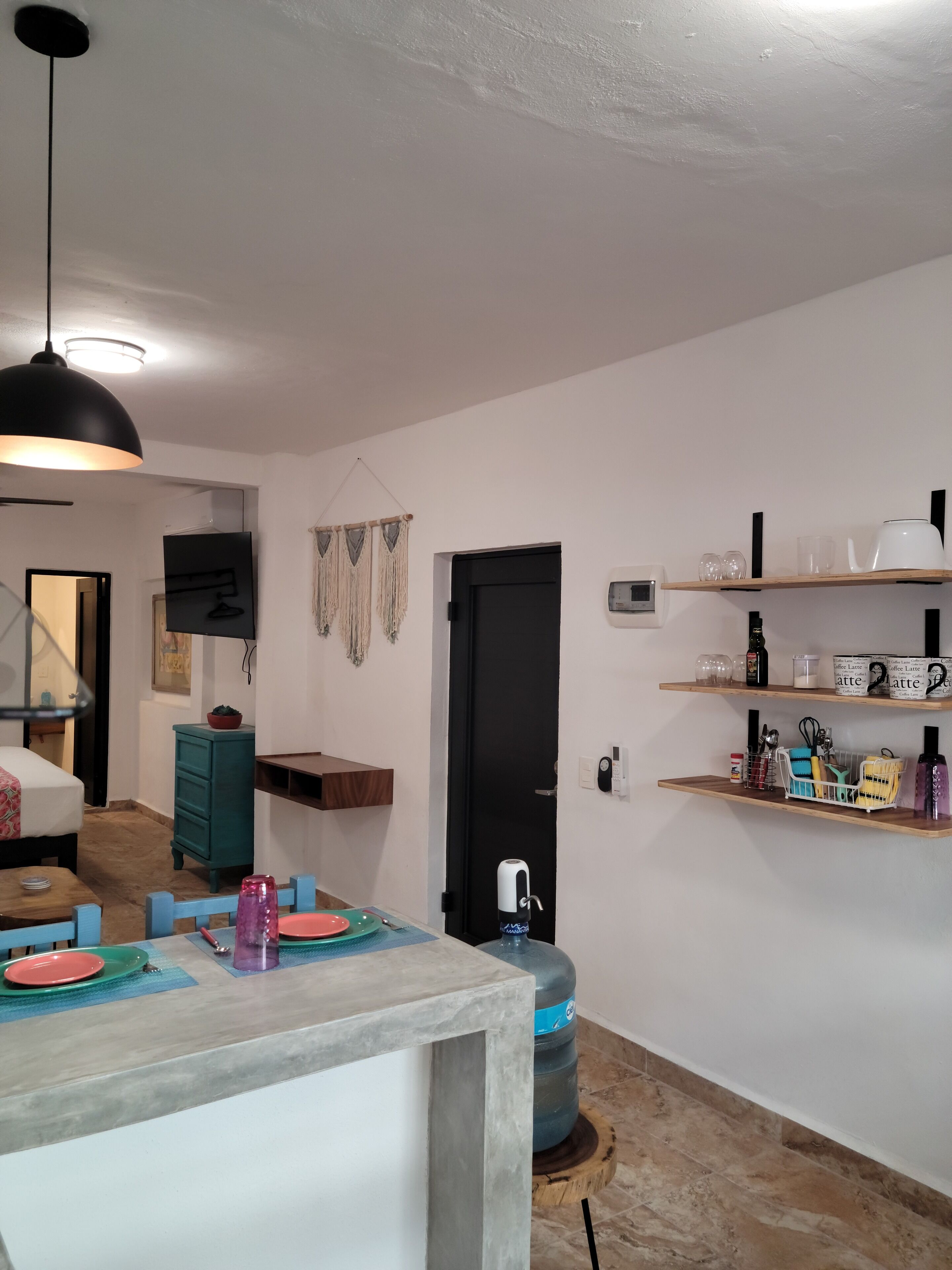 Cocina moderna con comedor, que incluye un dispensador de agua grande, una cafetera y estantes con utensilios de cocina.