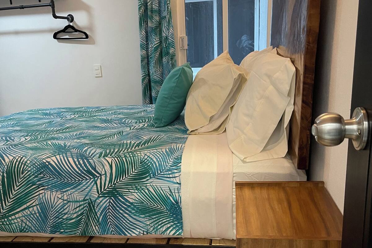 A bedroom with a bed, a wooden nightstand, a window with curtains, and a hanging light fixture.