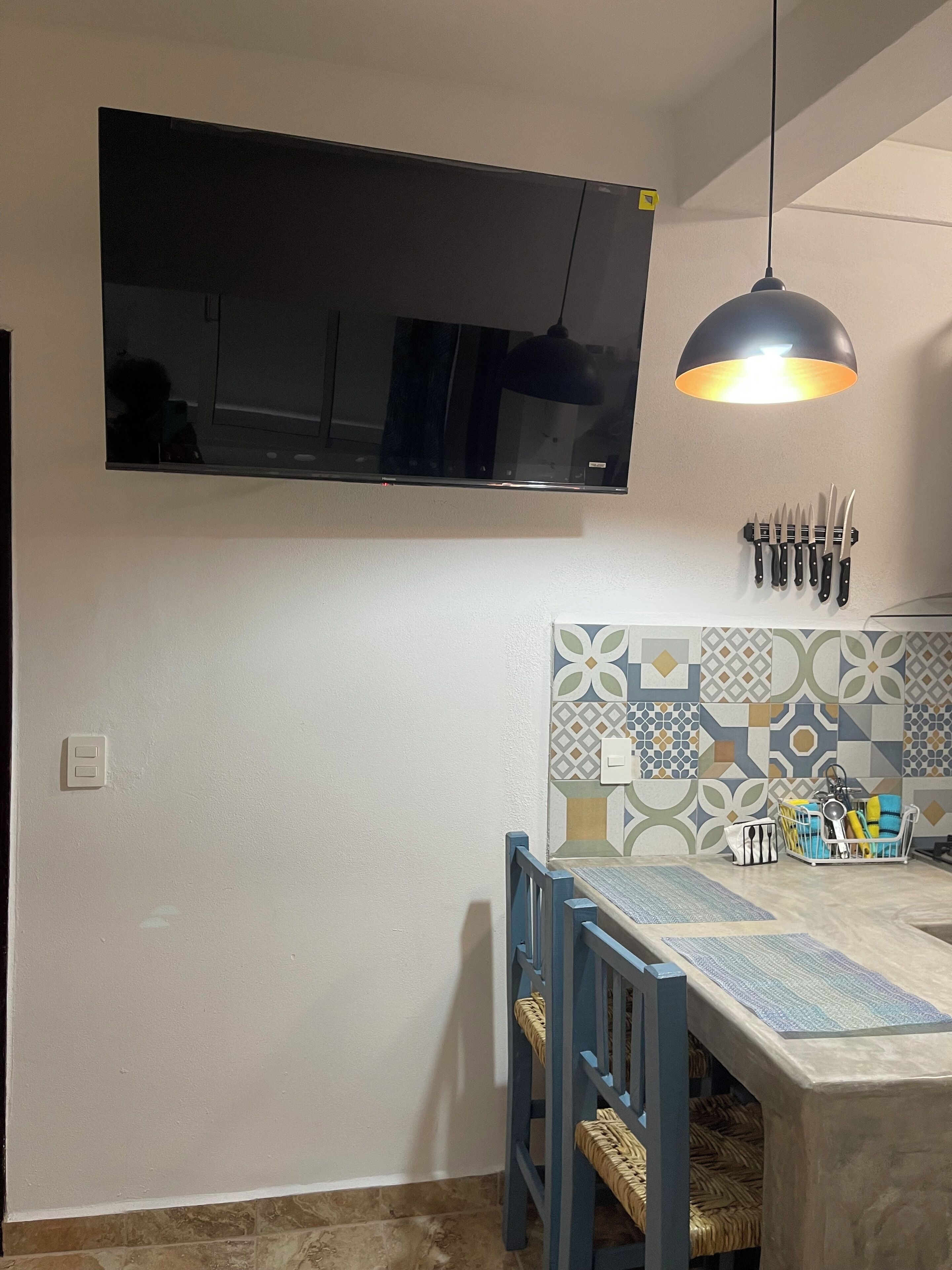 A kitchen with a TV mounted above the counter, a hanging pendant light, and a knife rack.