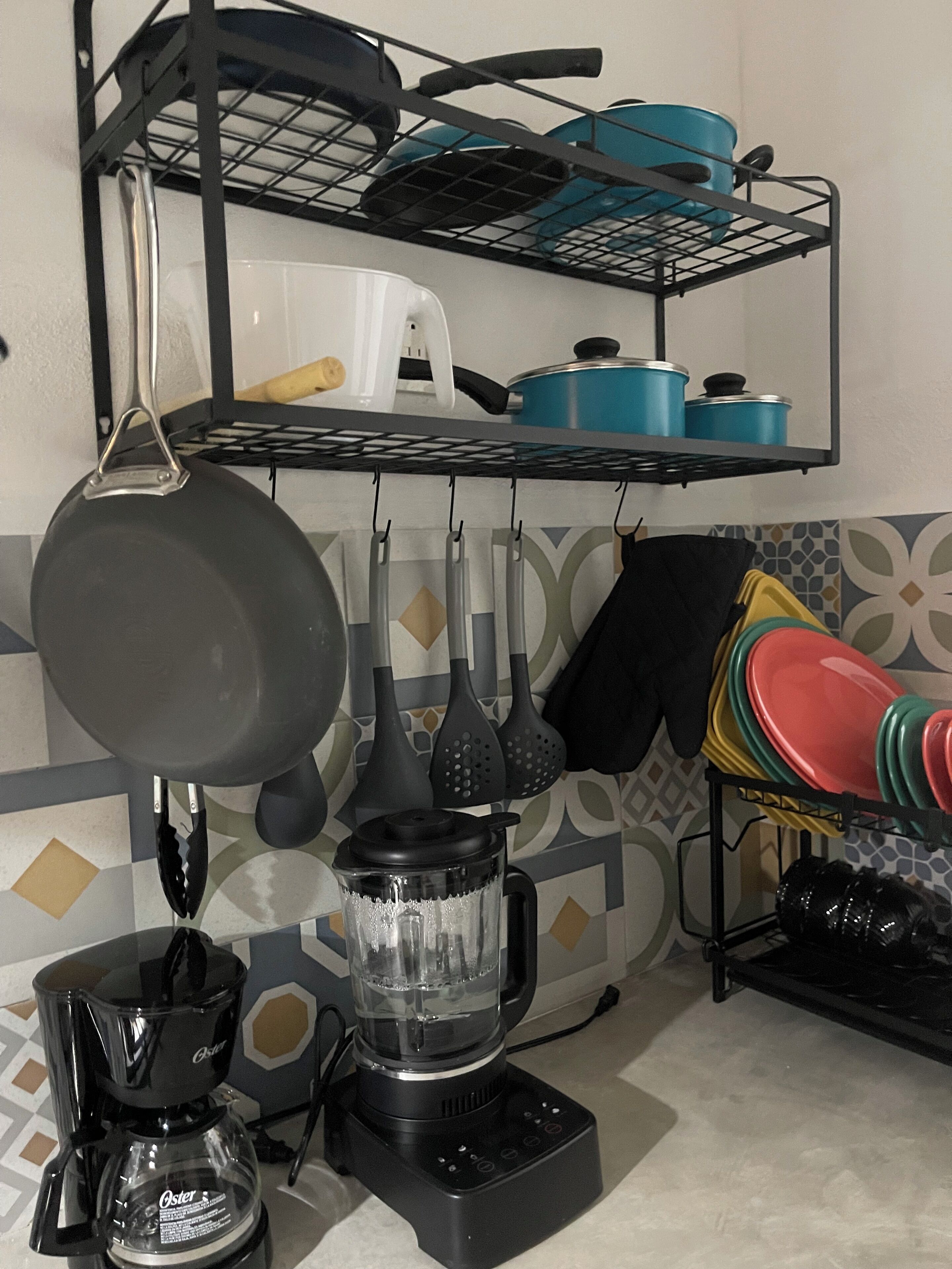 Cozinha com cafeteira, liquidificador, utensílios pendurados e prateleiras com panelas e frigideiras.