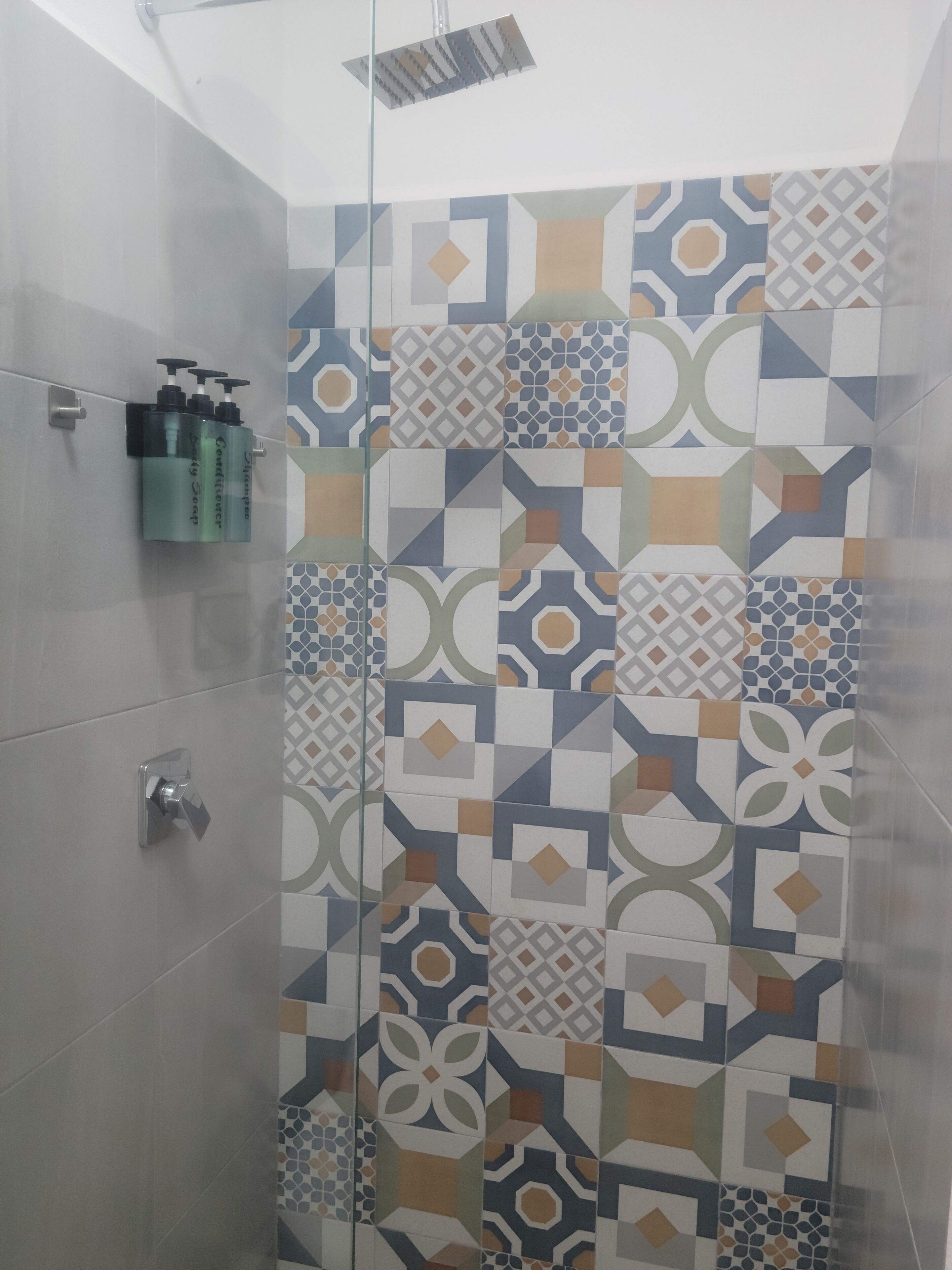 A shower area with a geometric tile pattern, a glass shower enclosure, and a shampoo dispenser on the wall.