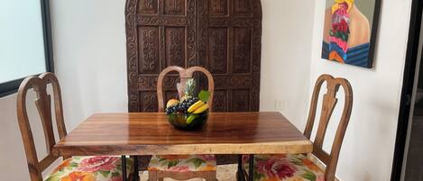 Una mesa de madera para comer con un frutero en el centro, rodeada de sillas de madera con tapicería floral.