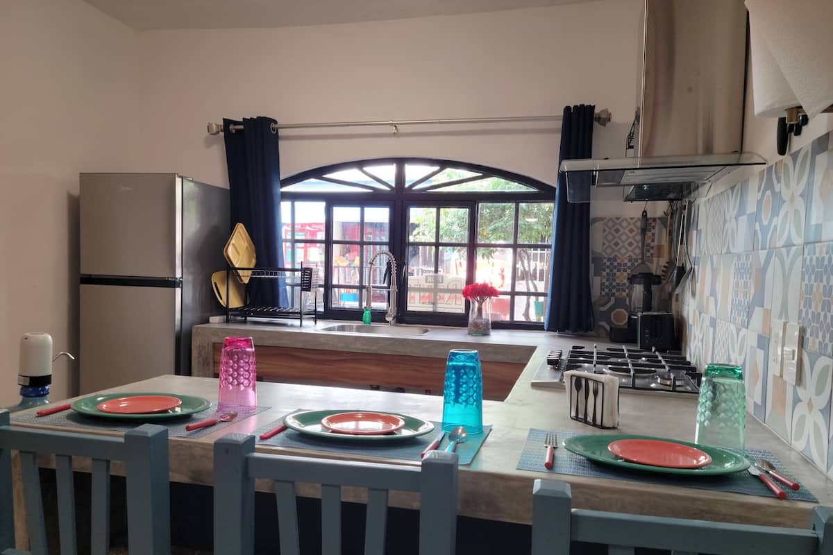 A kitchen with a dining area, a refrigerator, a sink, and a window with curtains.