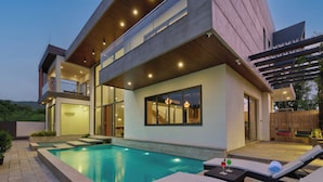 Una casa moderna con piscina, mobiliario exterior y un amplio ventanal con vistas a la piscina.