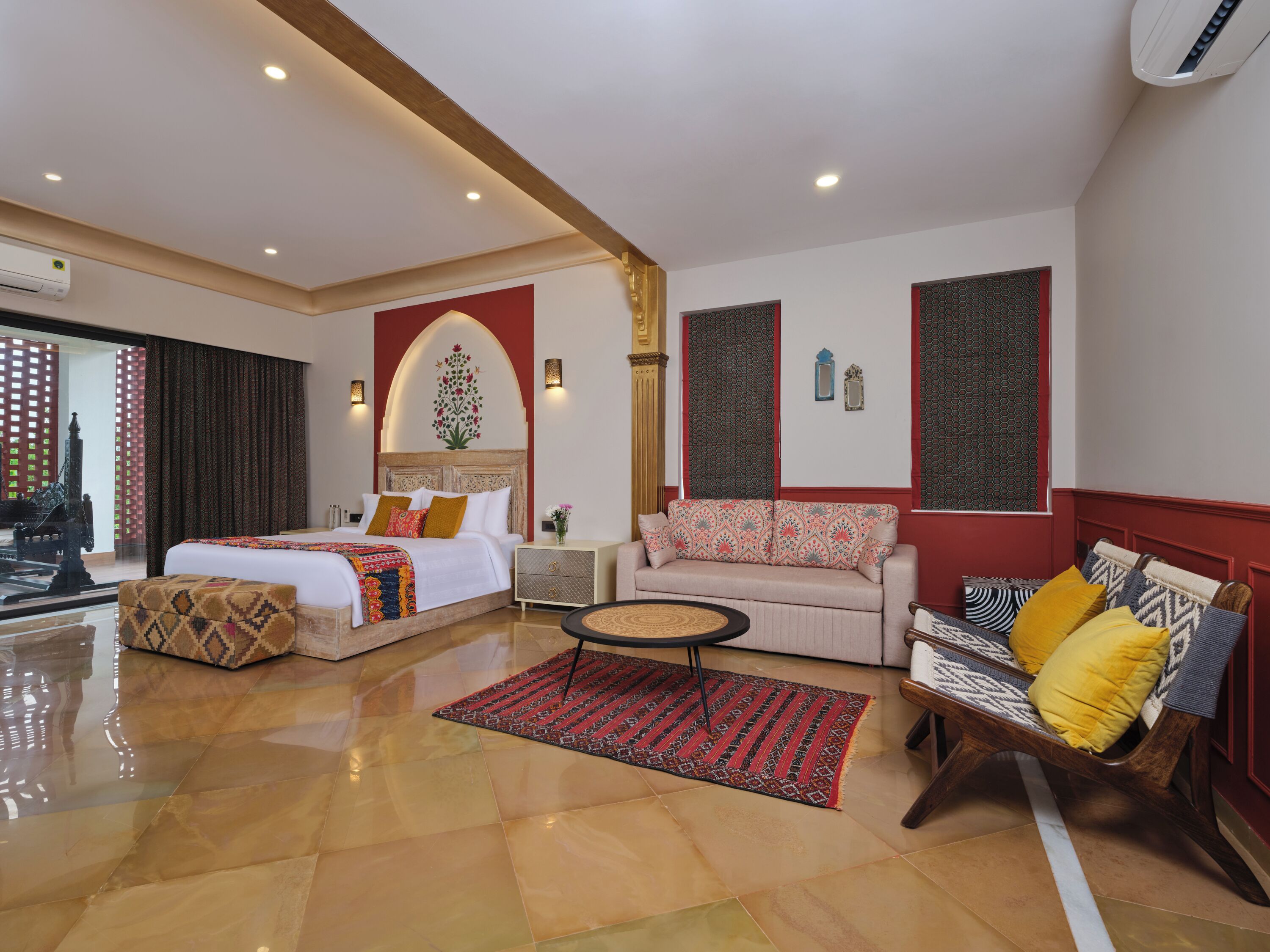 A spacious hotel room with a large bed, a sofa, a coffee table, and a patterned rug.