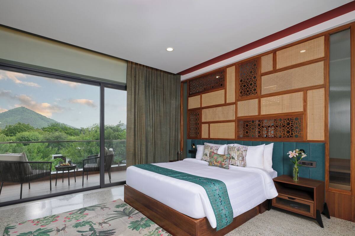 Un dormitorio con una cama grande, vistas a zonas verdes y un balcón con sillas.