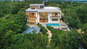 Una casa moderna de dos pisos con un amplio frente de vidrio, una piscina y un jardín exuberante.