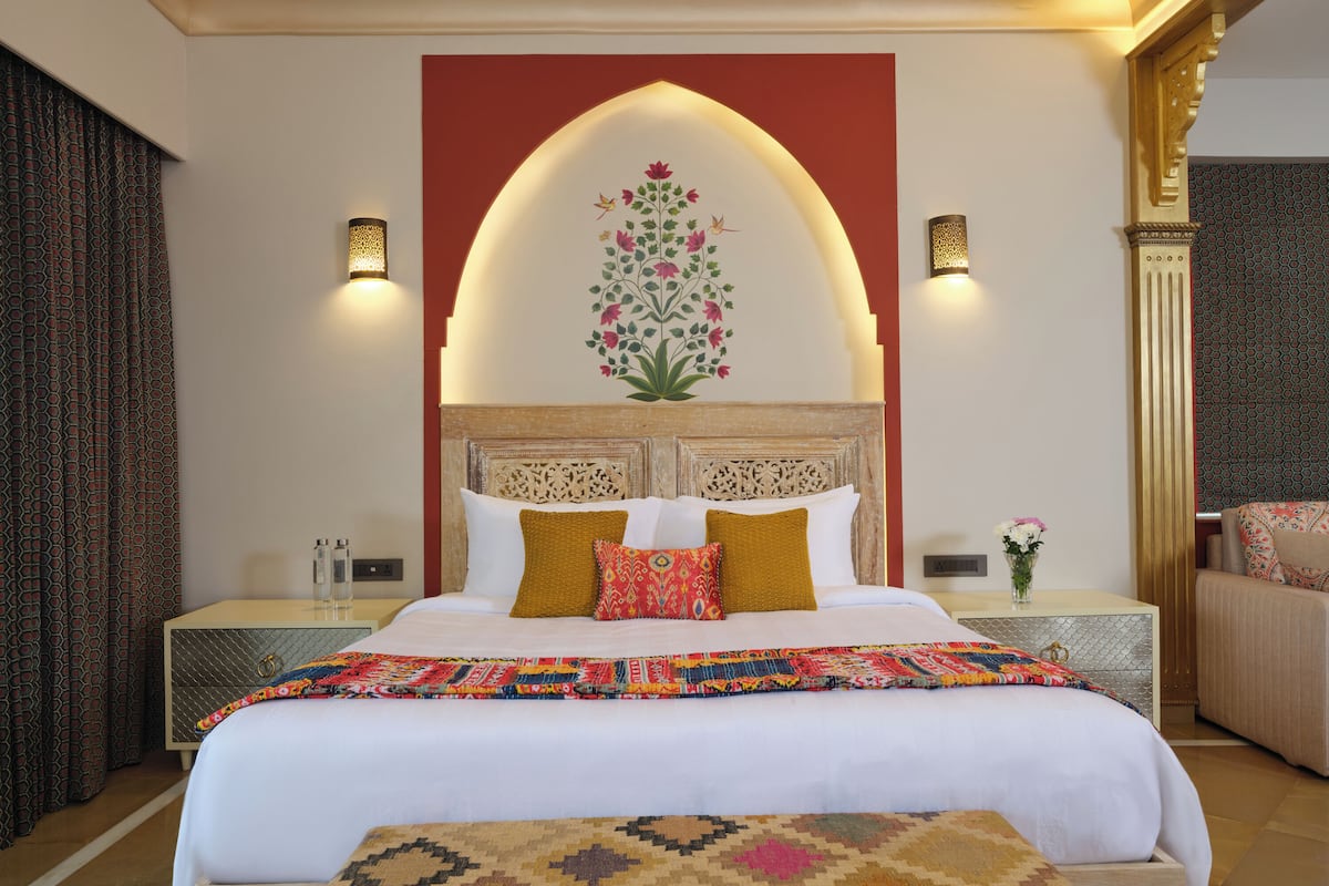 Un dormitorio bien iluminado con una cama grande, almohadas decorativas, una colcha estampada y una lámpara fijada a la pared.