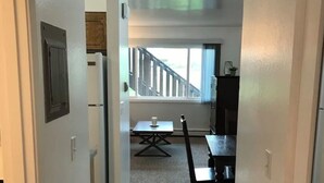 A narrow hallway leading to a dining area with a table and chairs, a window with a view of a staircase, and a refrigerator. - Ground Floor End Unit in Midtown Anchorage (Anchorage)