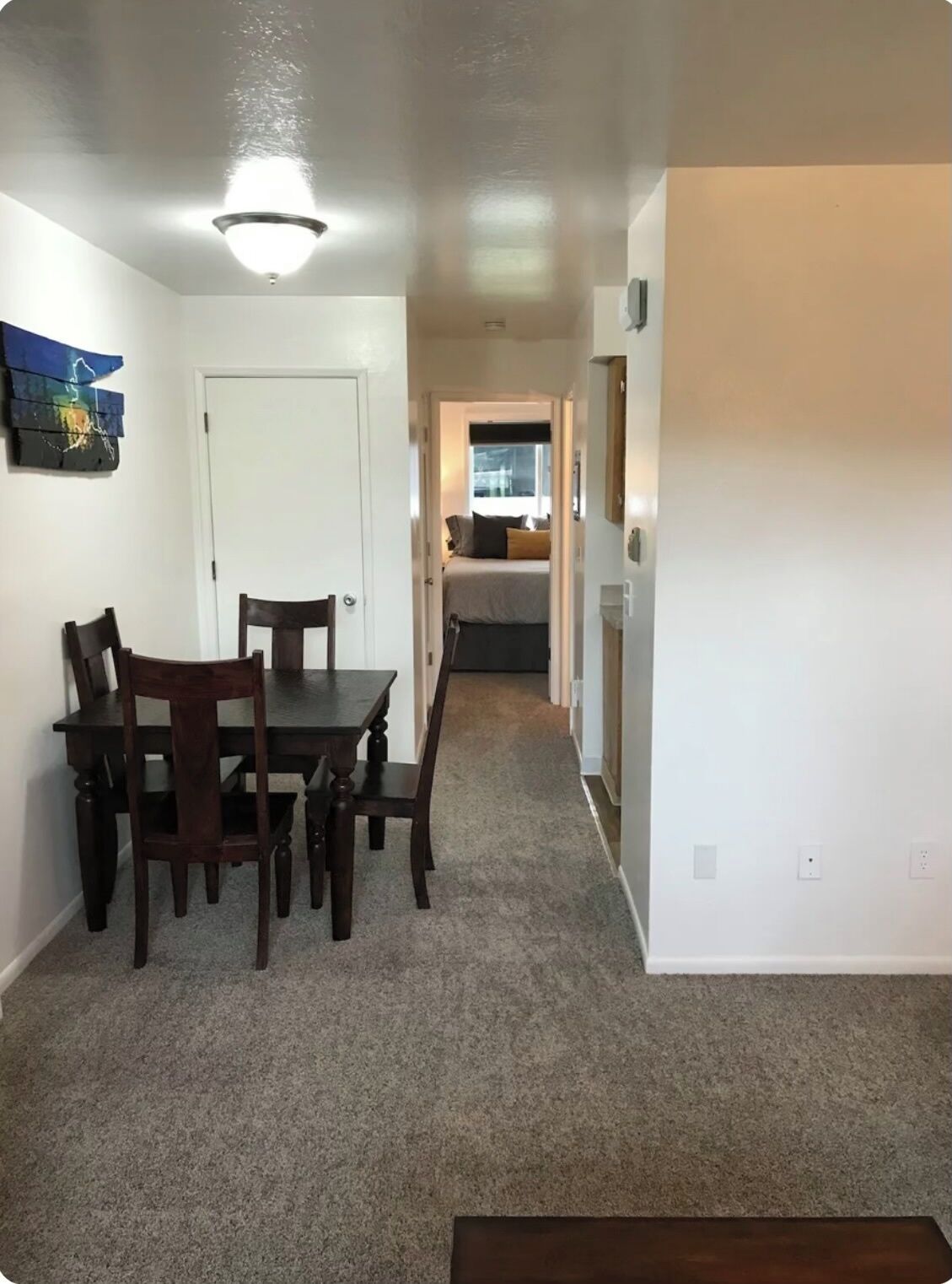 Un pasillo con una mesa de comedor y sillas, una puerta y una zona de cocina visible a través de otra puerta abierta.
