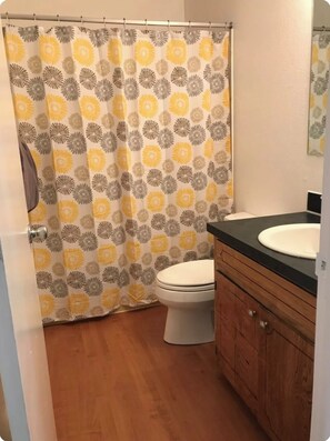 A bathroom with a shower curtain featuring a floral pattern, a white toilet, and a wooden vanity with a black countertop. - Ground Floor End Unit in Midtown Anchorage (Anchorage)