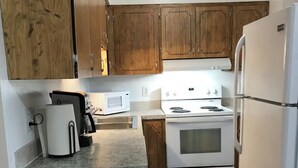 A compact kitchen with wooden cabinets, a white refrigerator, a microwave, and a stove. - Ground Floor End Unit in Midtown Anchorage (Anchorage)