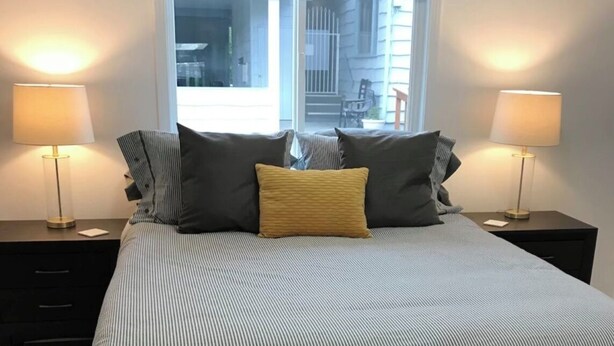 A neatly made bed with striped bedding, two bedside lamps, and a window with a view of the outside. - Ground Floor End Unit in Midtown Anchorage (Anchorage)