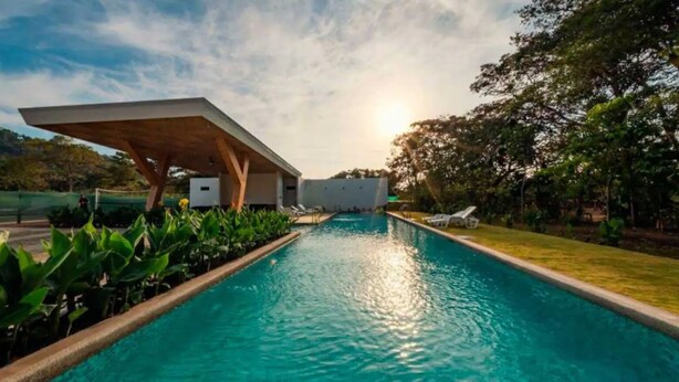 A swimming pool with a modern architectural structure on one side and lush greenery surrounding it. - Jaco Oasis Beach House (Jaco, Garabito)