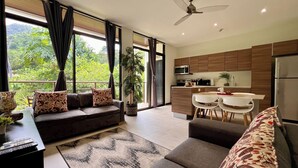 A modern living room with a sofa, a dining area with a table and chairs, a kitchen with a microwave and stove, and a ceiling fan. - Jaco Oasis Beach House (Jaco, Garabito)