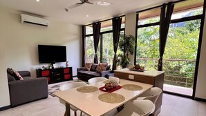 A modern living room with a dining area, large windows, and a ceiling fan. - Jaco Oasis Beach House (Jaco, Garabito)