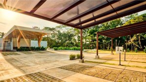 A covered outdoor area with a modern pavilion structure, a paved walkway, and surrounding greenery. - Jaco Oasis Beach House (Jaco, Garabito)