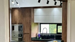 A modern kitchen with wooden cabinetry, a built-in oven, a sink, and bar stools. - Villa Privada eje Cafetero (Quindío)