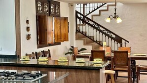 A modern kitchen with a central island, wooden cabinets, and a dining area with a staircase. - Villa Privada eje Cafetero (Quindío)
