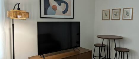 A room with a flat-screen TV mounted on a wooden cabinet, a floor lamp, and three stools.
