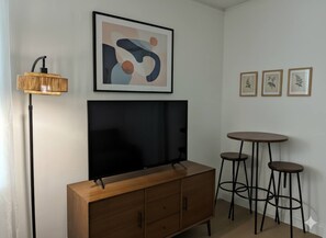 A room with a flat-screen TV mounted on a wooden cabinet, a floor lamp, and three stools.