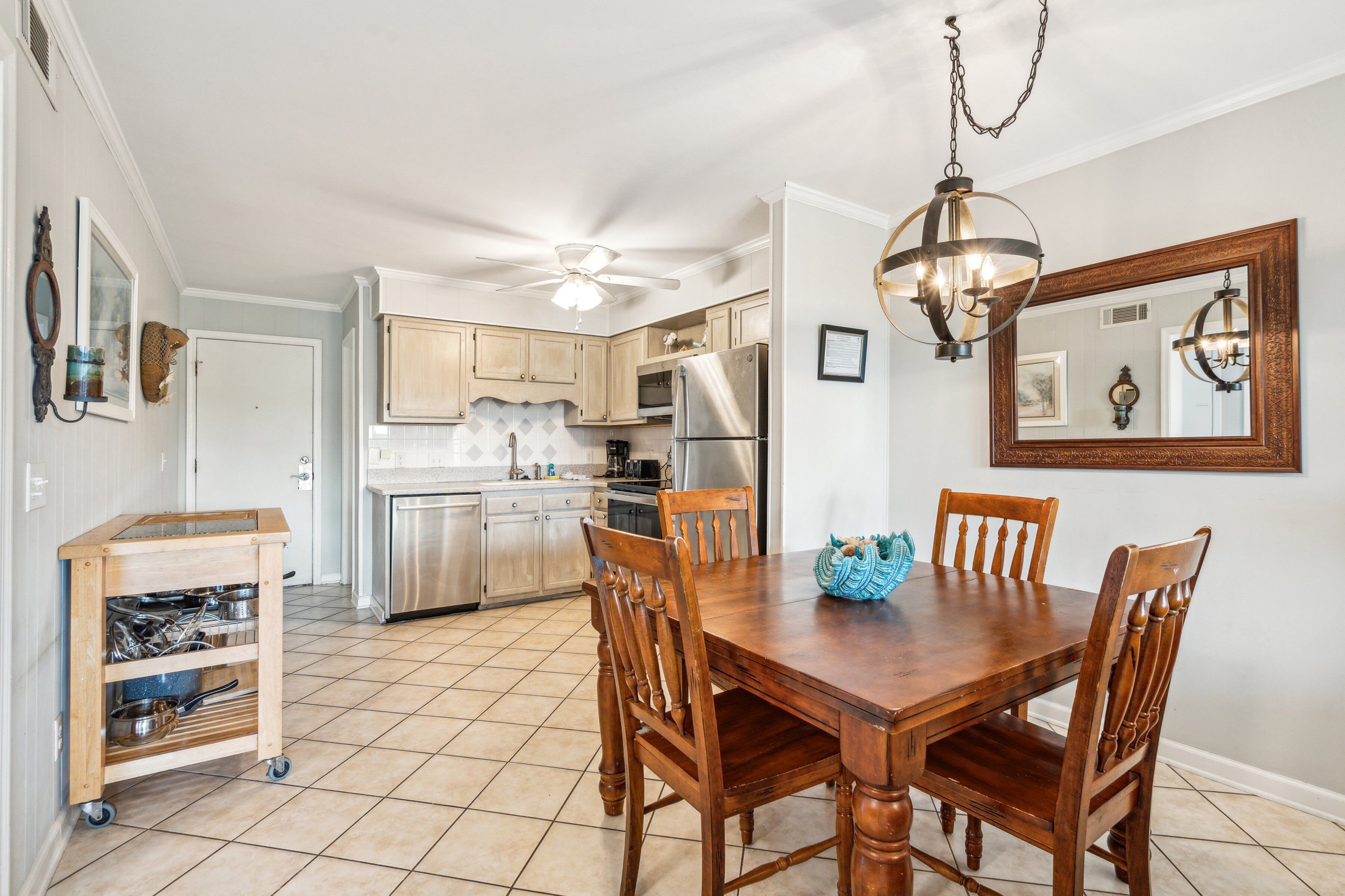 A dining area with a wooden table and chairs, a ceiling fan, and a kitchen in the background.