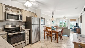 A modern kitchen with stainless steel appliances, a dining area with wooden furniture, and a ceiling fan. - Top Floor condo, Pool, across from Beach & Pier Access! - 310C Oceanside (Isle Of Palms)