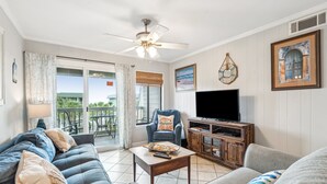 A living room with a sofa, armchair, coffee table, TV, and artwork. - Top Floor condo, Pool, across from Beach & Pier Access! - 310C Oceanside (Isle Of Palms)