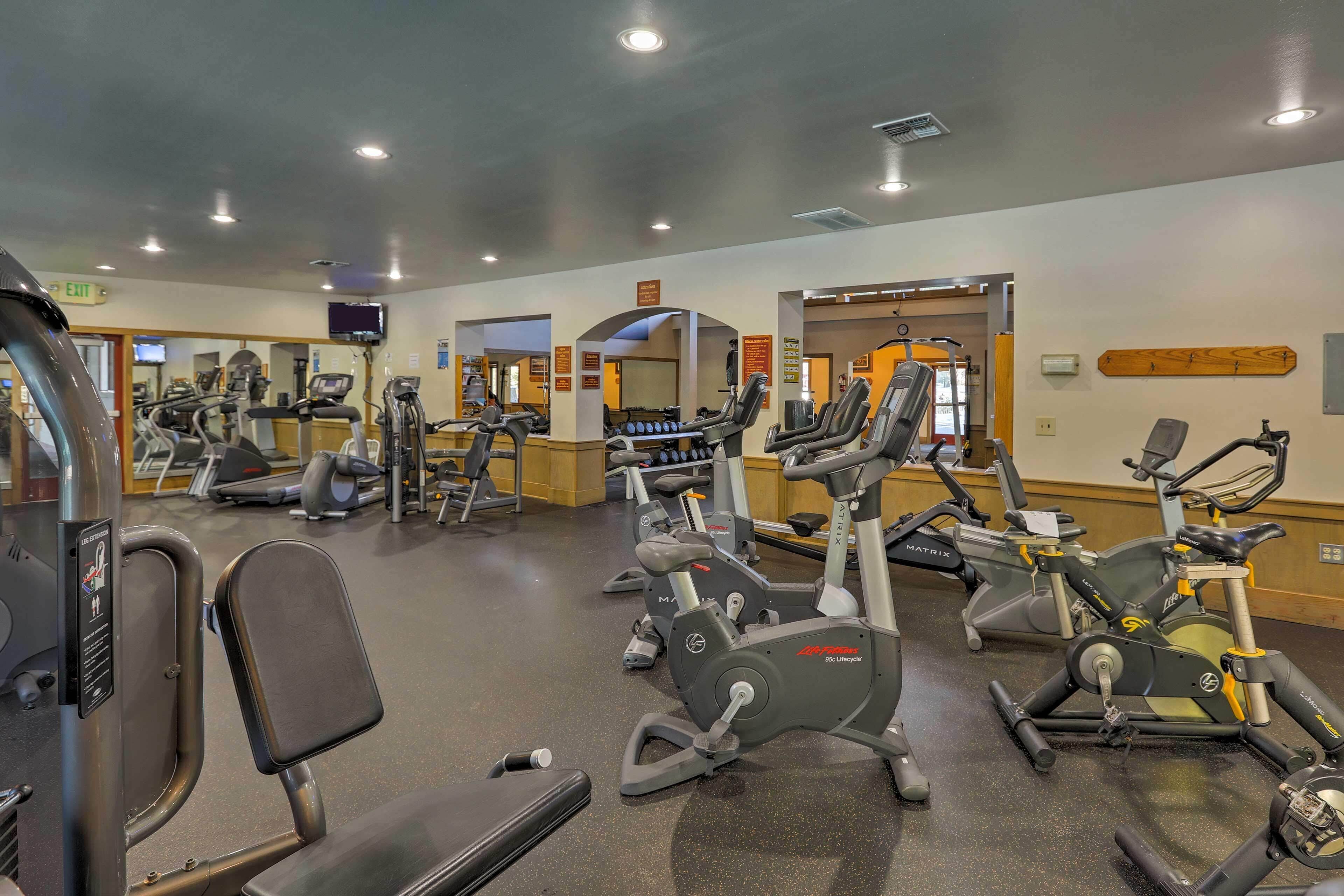A gym with various exercise machines, mirrors, and a television screen.