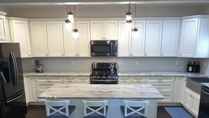 A modern kitchen with white cabinets, a central island with bar stools, stainless steel appliances, and pendant lighting. - Pool, Pet Friendly, Close to Beach (Cape May)