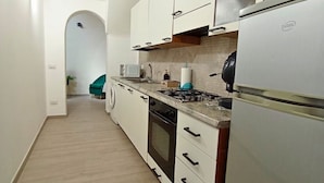 A compact kitchen with white cabinets, a gas stove, a microwave, and a refrigerator.