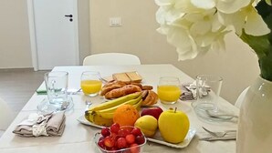 A dining table set with fruits, pastries, and juice glasses, with a vase of flowers on the right.