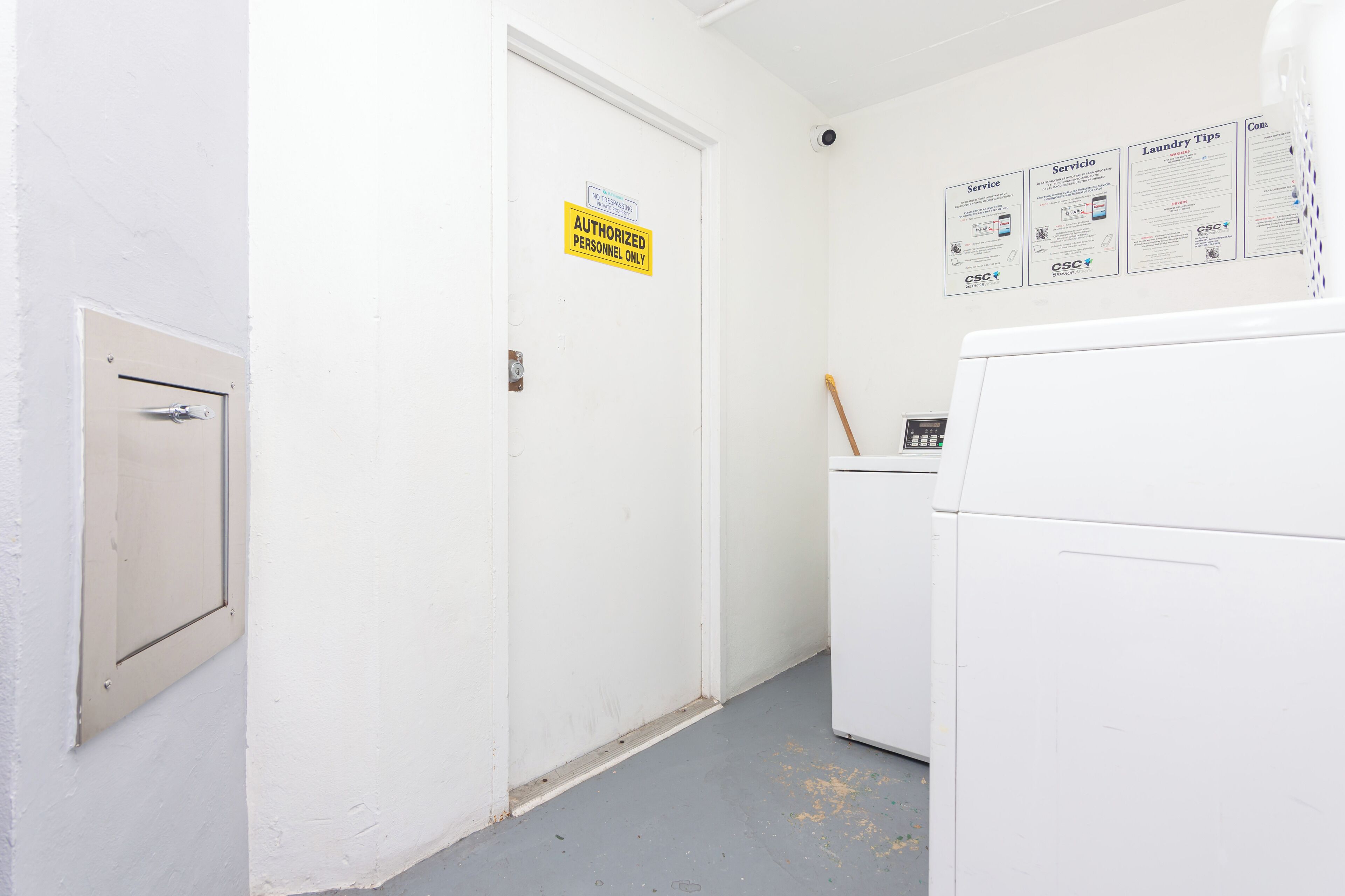 A laundry room with a door marked "Authorized Personnel Only," a washing machine, and informational posters on the wall.