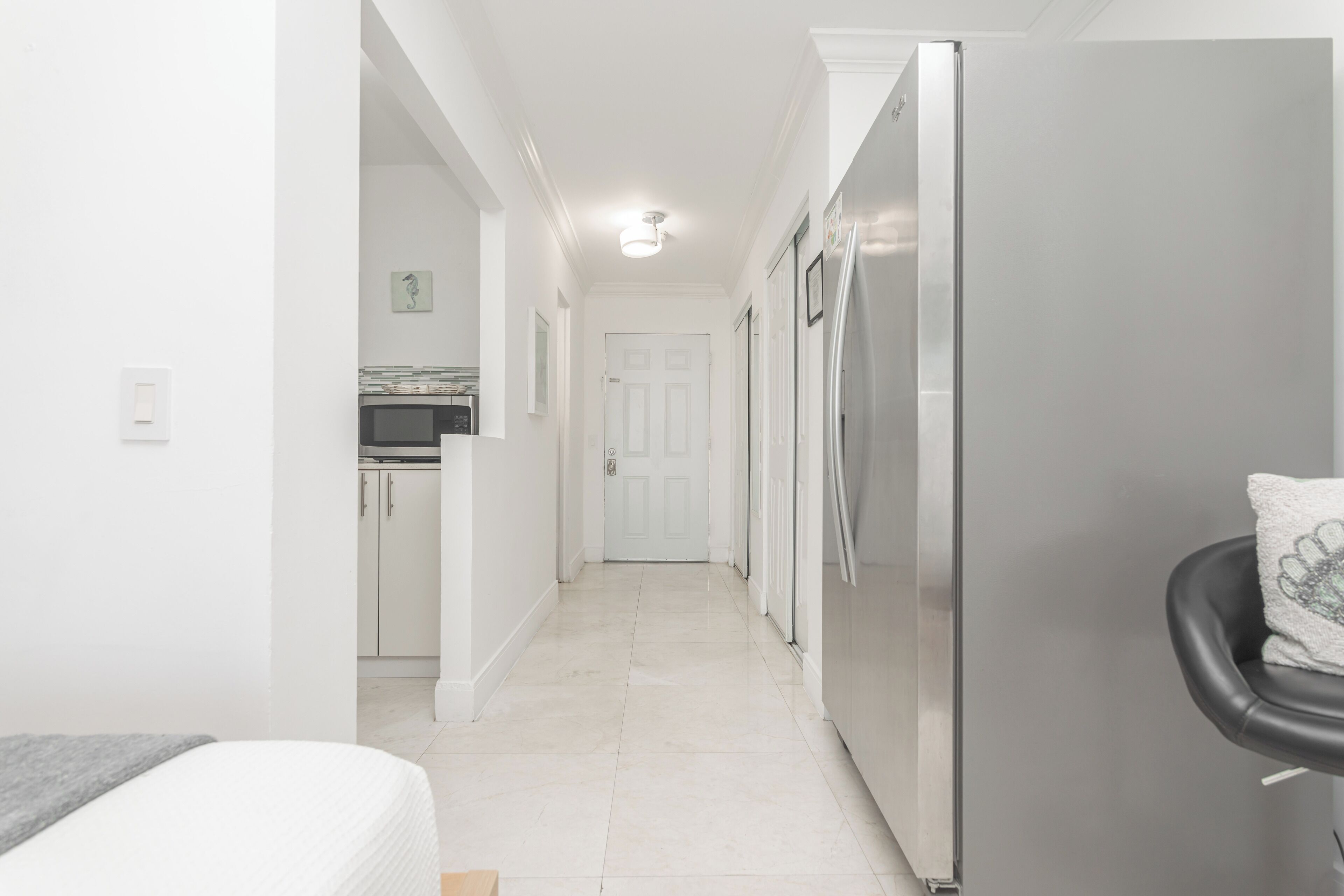 Un pasillo estrecho con una zona de cocina a la izquierda, una puerta al final y un refrigerador a la derecha.