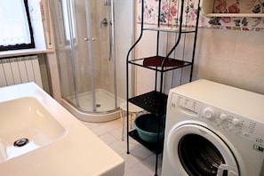 Une salle de bain avec une douche, un lavabo et un lave-linge.