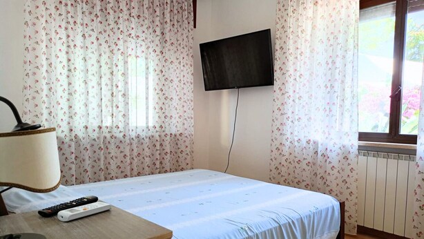 A bedroom with a bed, a TV mounted on the wall, a window with curtains, and a radiator. - SE115 - Marotta, comfortable two-room apartment with parking (Marotta)