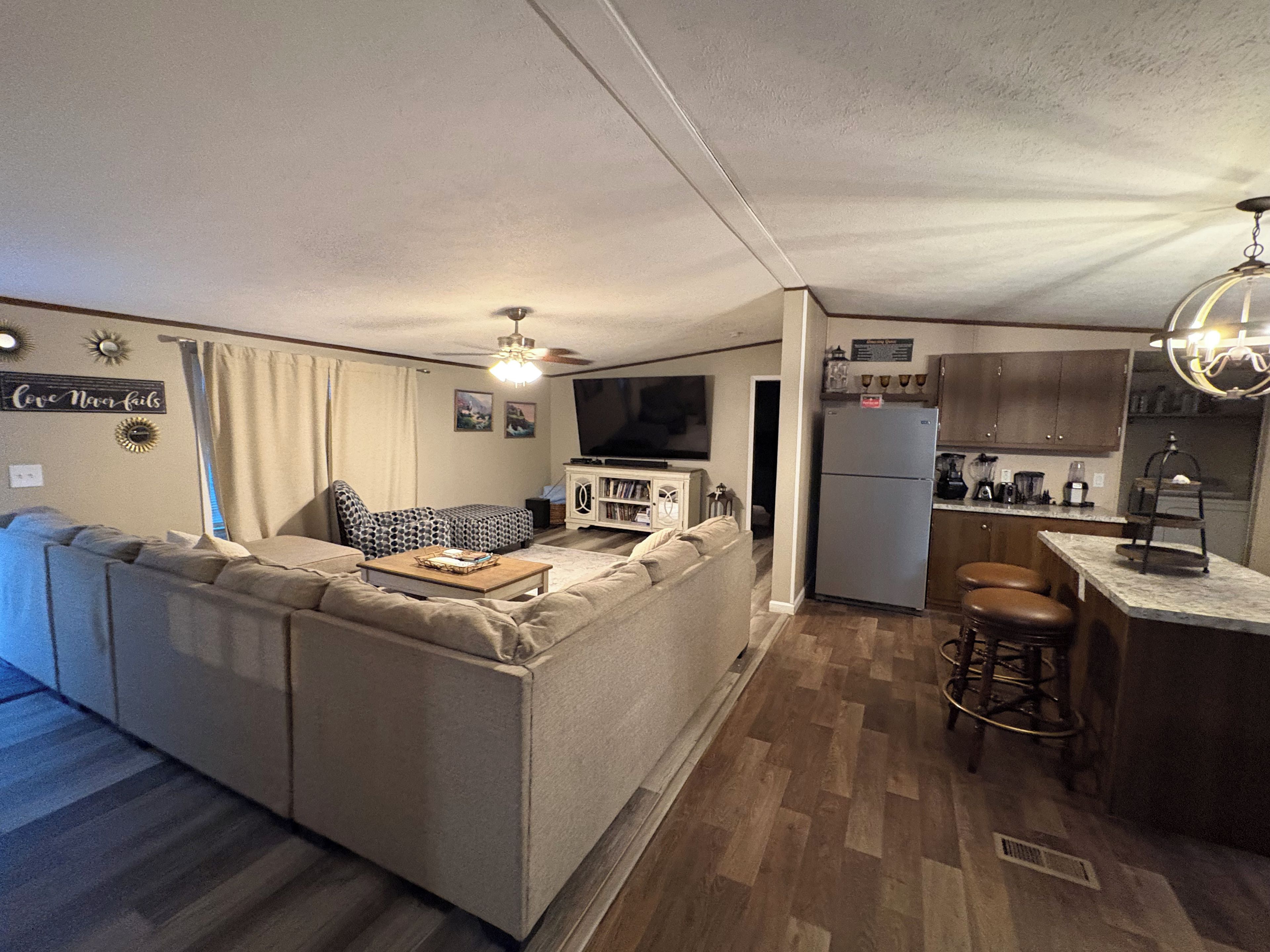 A compact living space with a sofa, a television, a refrigerator, and a kitchen area with stools.