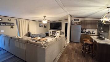 A compact living space with a sofa, a television, a refrigerator, and a kitchen area with stools.