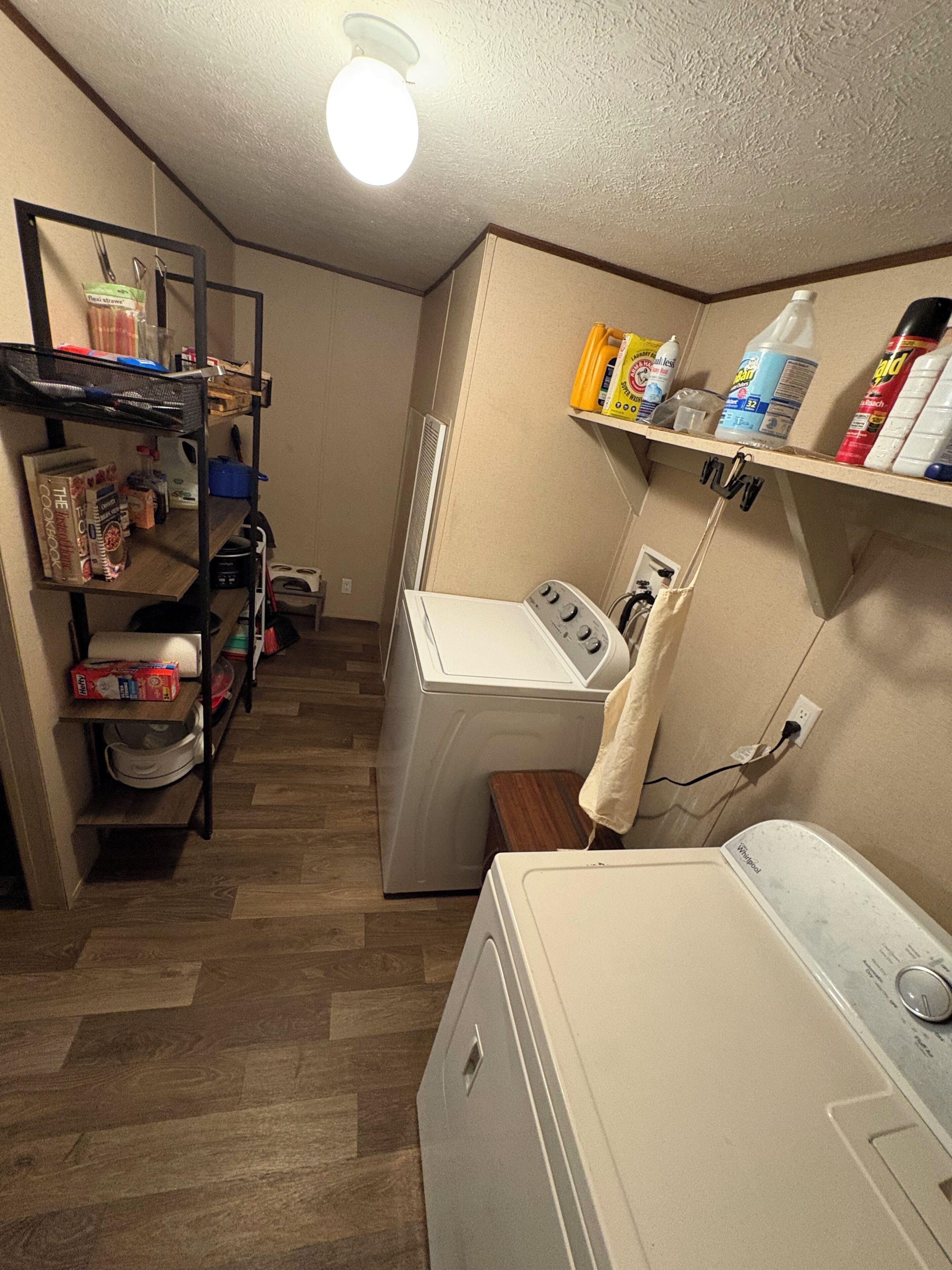 A laundry room with a washing machine, dryer, shelves with cleaning supplies, and a rack with various items.