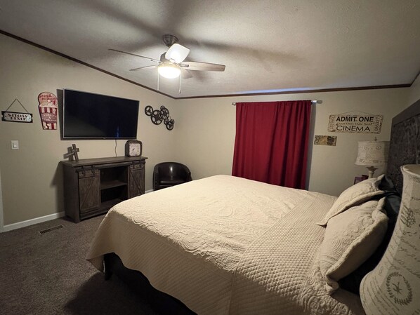 Un dormitorio con cama, ventilador de techo, televisor, reloj y un cartel en la pared.