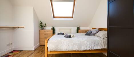 A bedroom with a wooden bed, a skylight, a dresser, and a small plant.