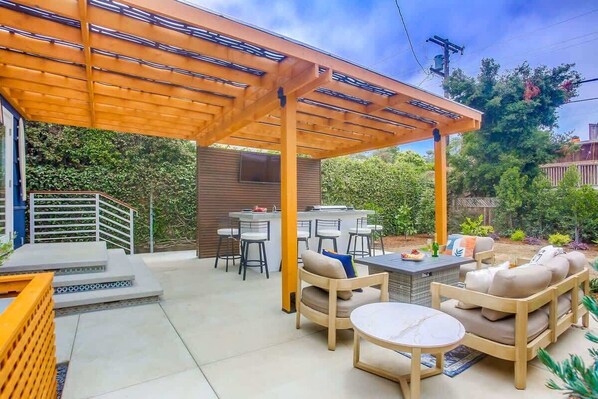 A covered patio area with a wooden pergola, outdoor seating, and a barbecue grill. - Windansea Beach House - beautifully updated 2BD (La Jolla)