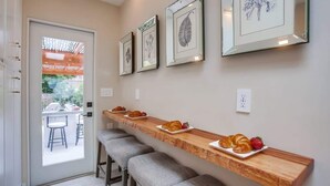 A kitchen with a wooden countertop, bar stools, and framed botanical prints on the wall. - Windansea Beach House - beautifully updated 2BD (La Jolla)
