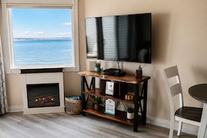 A living room with a fireplace, a television mounted on the wall, a wooden coffee table, and a view of the sea.
