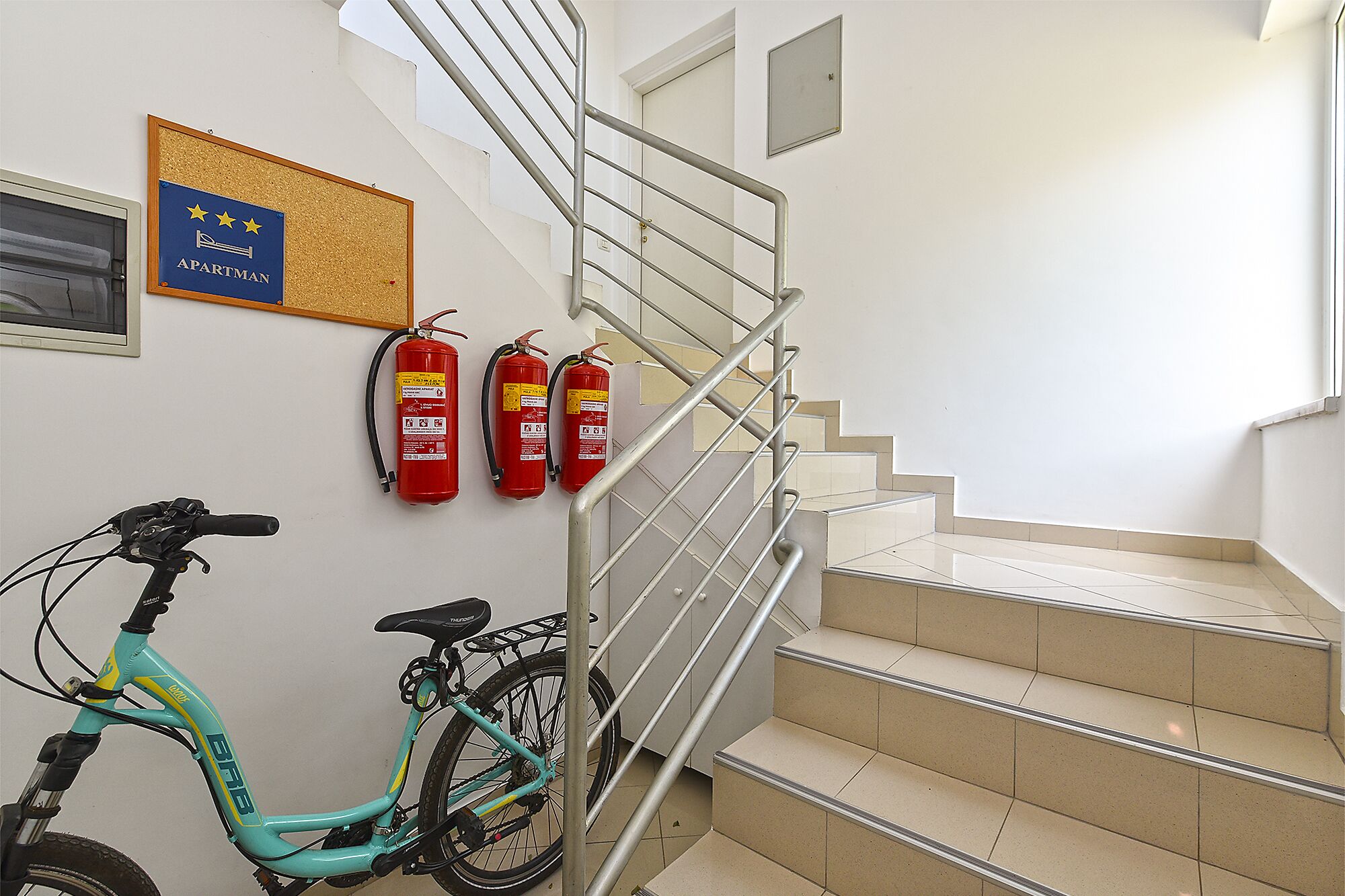 Una scala con ringhiere in metallo, un estintore montato a parete e una bicicletta appoggiata al muro.