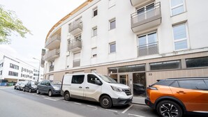 A multi-story building with a white facade, balconies, and a parking area with cars. - Appartement Crista - Welkeys (Saint-Denis)