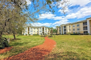 A pathway leading to a building with multiple balconies and a well-maintained lawn.