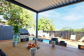 Un patio al aire libre con piscina, sillones de descanso y una mesa de comedor con comida y bebidas.
