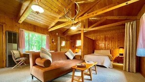 A cozy cabin interior with a sofa, a bed, and a dining table. - TATA River Cabins- group getaway (Salida)